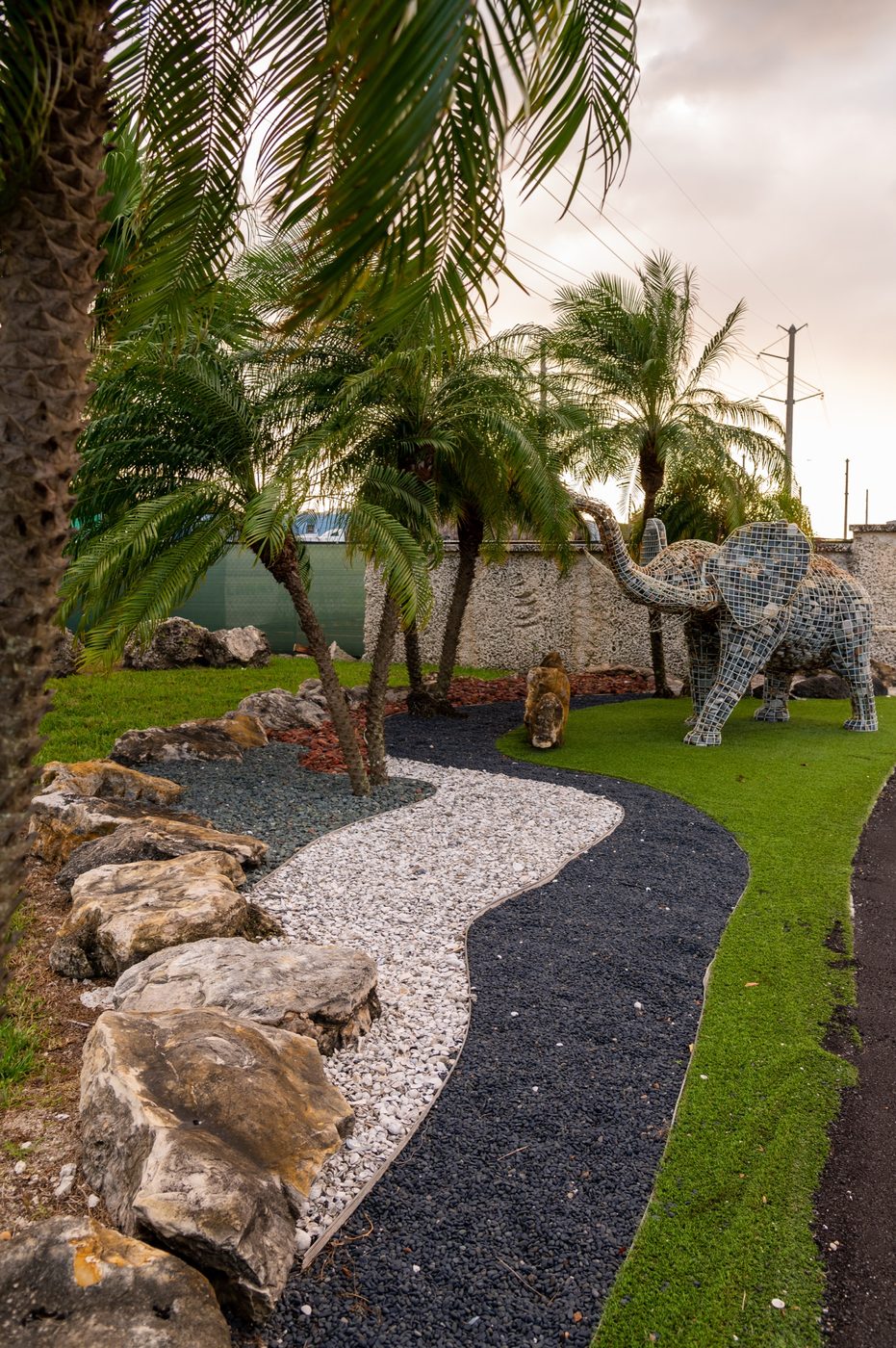Landscaped display garden at Olimar Stone with palms, boulders and a black pebble path